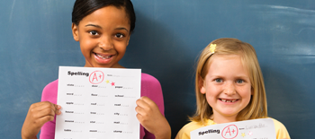 Two young girls smiling and holding up their homework with an A grade on it