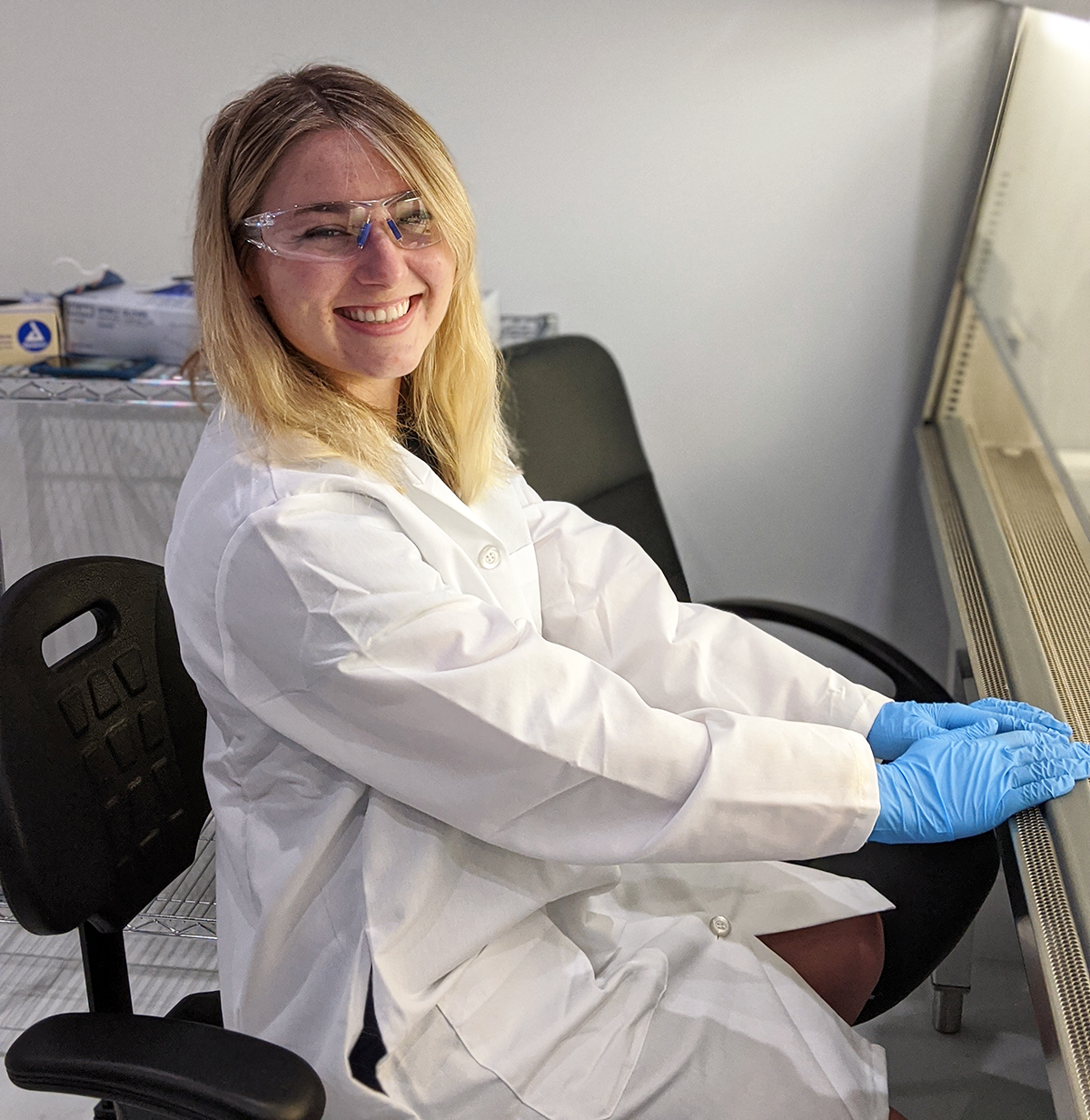 Student in a labcoat and lab setting smiling