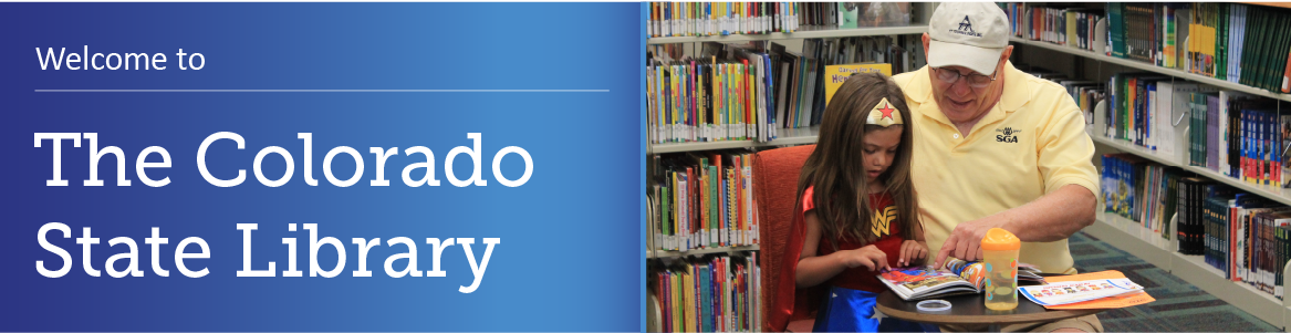 A child and an adult sitting at a table in the library reading a book together. 