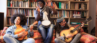 Three people lounging on a couch playing instruments in the library. 