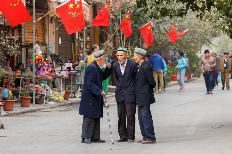 KASHGAR, XINJIANG / China - October 4, 2017: Three elderly men of the Uyghur minority having a conversation at a street in Kashgar Old Town. Chinese flags are mounted on the house in the background.