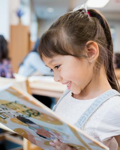 Young girl smiling at a book in a classroom setting