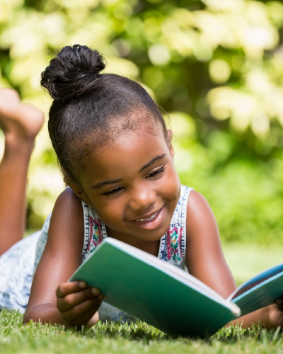 Smiling young girl reading a book outdoors on the grass