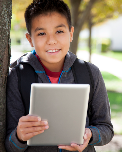 Young boy smiling and holding a personal computing device in an outdoor setting