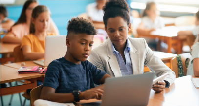 A child and an adult, seated, looking at a book together in a classroom. 